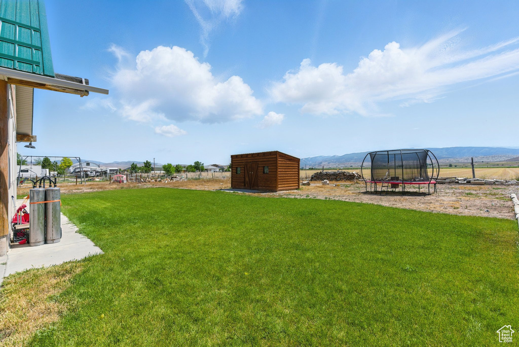 View of green lawn featuring a trampoline, a storage unit, and a mountain view