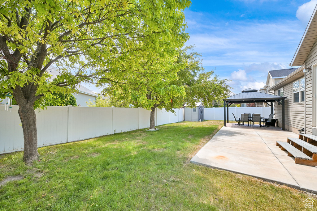 Fenced backyard featuring a gazebo, a patio area, and a storage shed