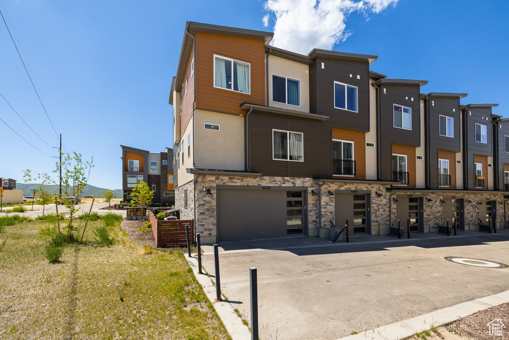 Back of house with stone siding, an attached garage, driveway, and a residential view