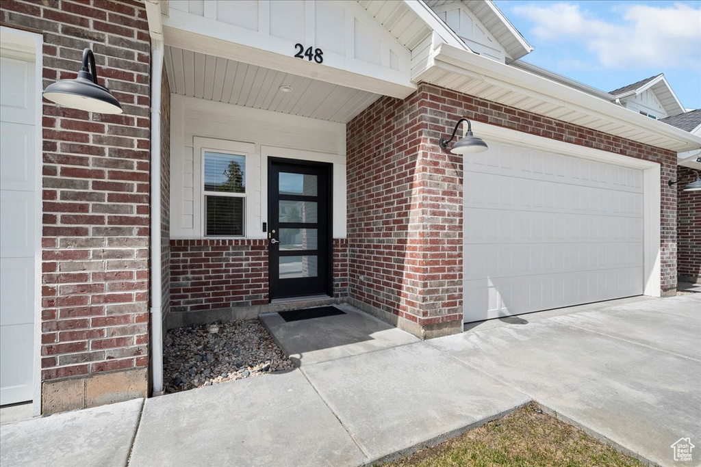 Doorway to property with brick siding, concrete driveway, and a garage