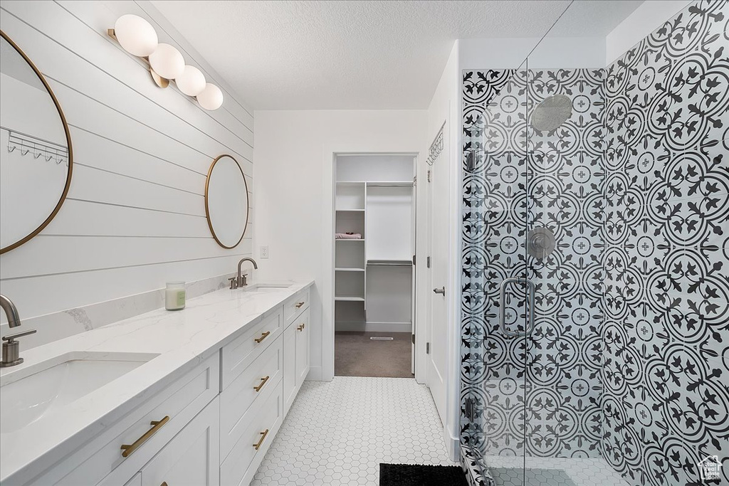 Bathroom featuring tiled shower, double vanity, a textured ceiling, tile patterned floors, and a spacious closet