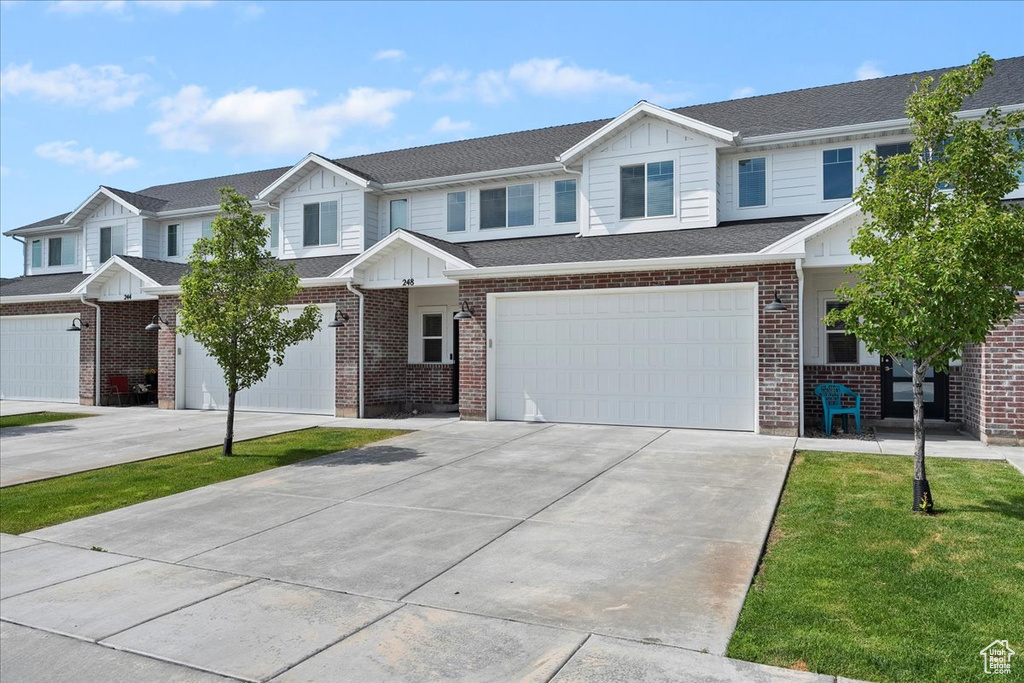 Multi unit property with board and batten siding, driveway, an attached garage, and brick siding