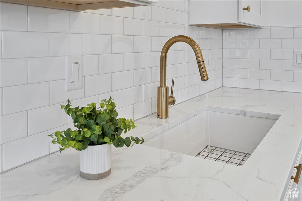 Kitchen view of backsplash, light stone counters, and white cabinetry