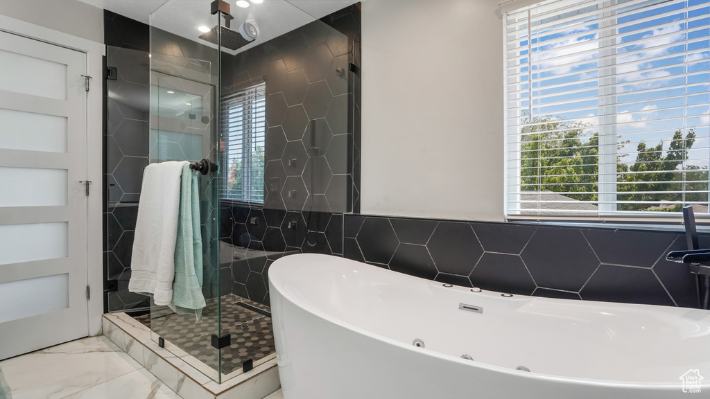 Bathroom featuring tile walls, a soaking tub, a stall shower, healthy amount of natural light, and marble look tiles