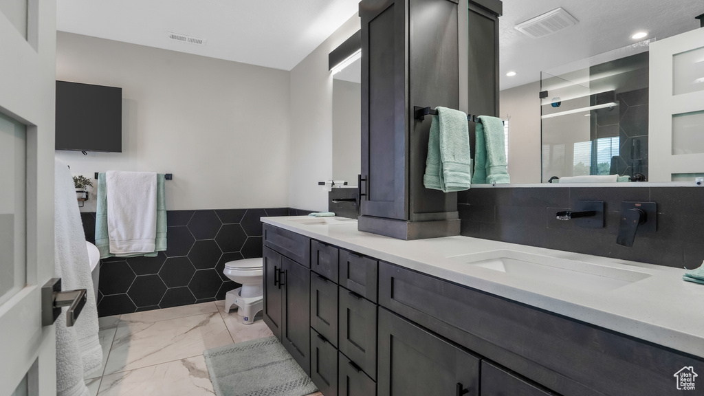 Bathroom with double vanity, a shower stall, tile walls, a wainscoted wall, and marble look tiles