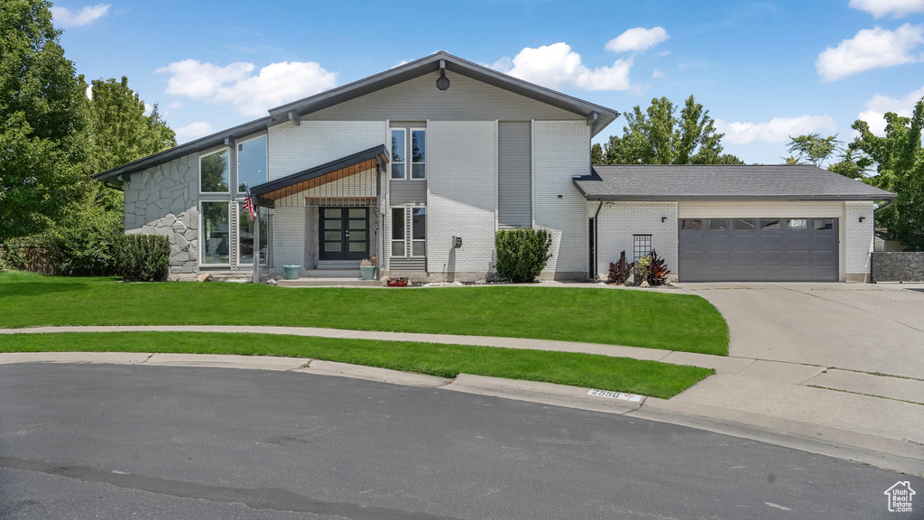 View of front of home featuring an attached garage, a front lawn, driveway, brick siding, and french doors