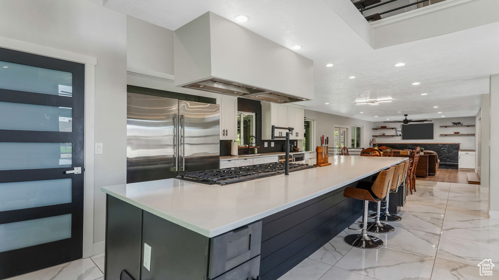 Kitchen featuring stainless steel built in fridge, light marble finish flooring, recessed lighting, stovetop, and white cabinets