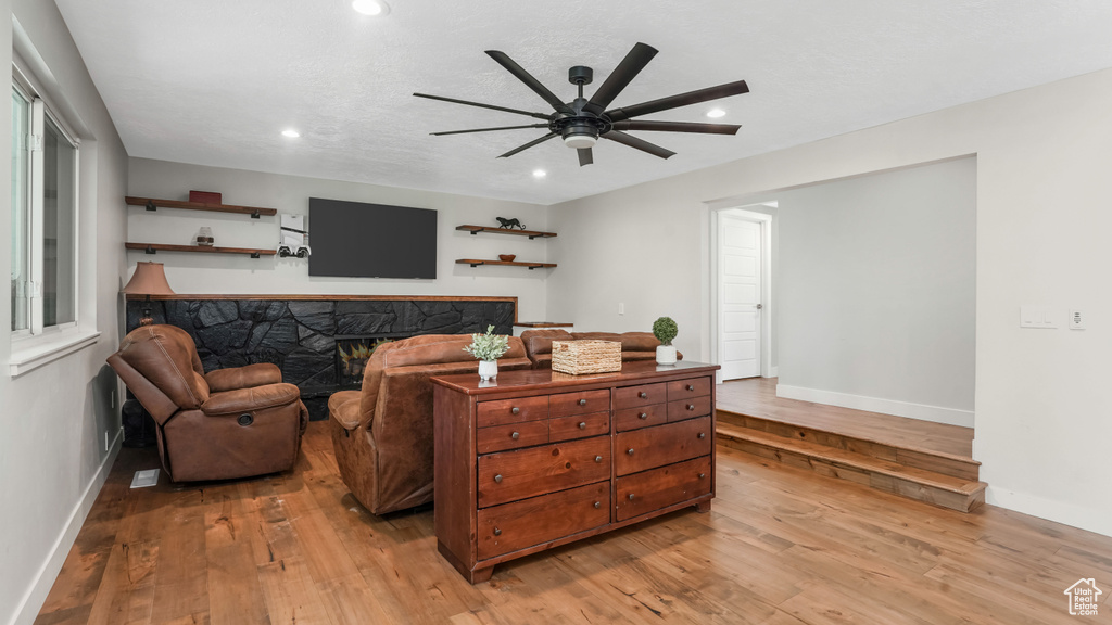 Living area with light wood-style floors, a ceiling fan, recessed lighting, and a stone fireplace