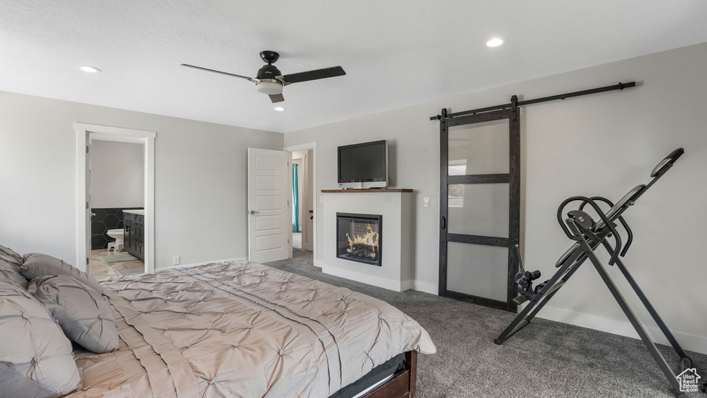 Carpeted bedroom with a barn door, a glass covered fireplace, recessed lighting, a ceiling fan, and ensuite bath