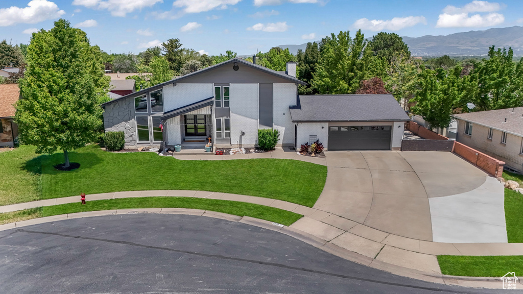 View of front of house with driveway, an attached garage, a front yard, and a mountain view