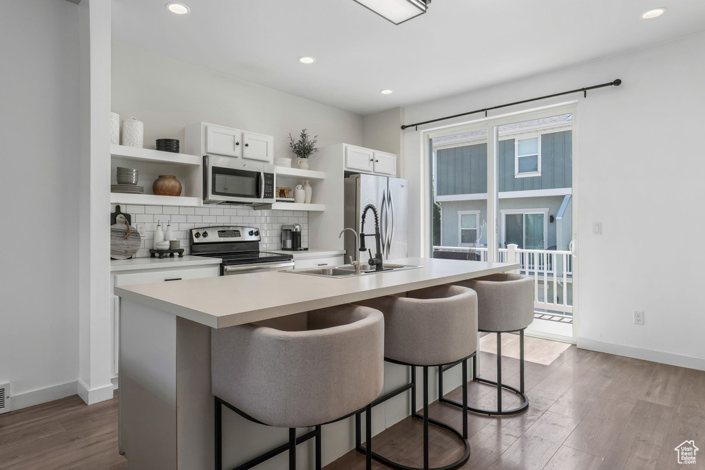 Kitchen with appliances with stainless steel finishes, open shelves, dark wood finished floors, a kitchen bar, and recessed lighting