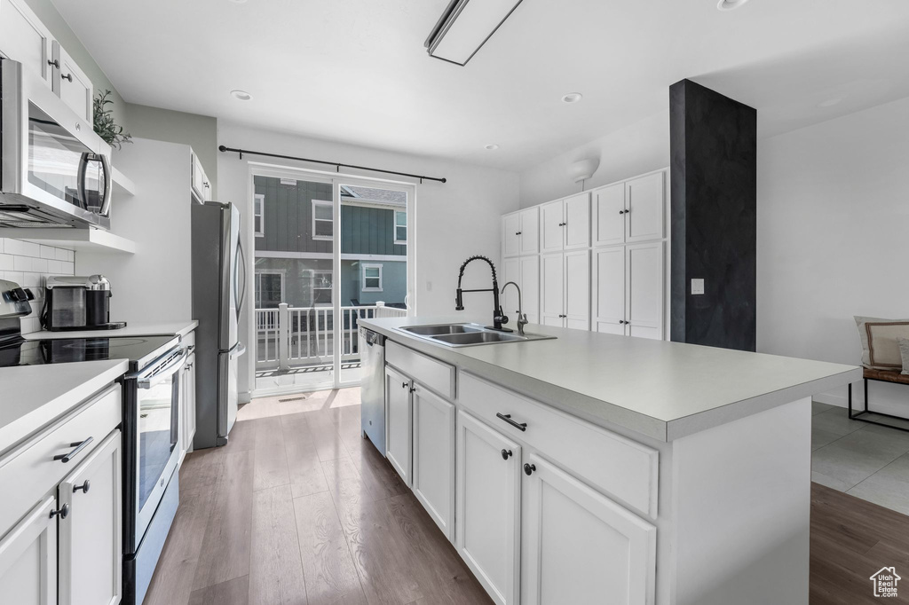 Kitchen featuring stainless steel appliances, light countertops, white cabinetry, wood finished floors, and recessed lighting