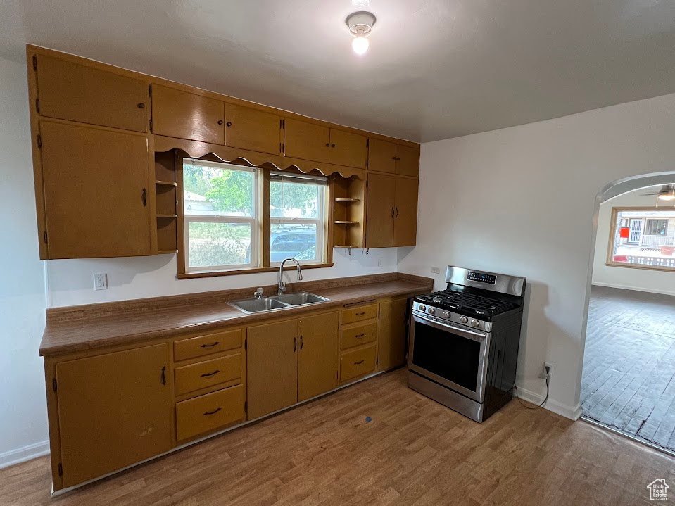 Kitchen featuring stainless steel range with gas cooktop, open shelves, light wood finished floors, and arched walkways