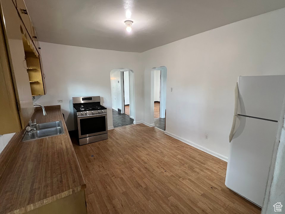 Kitchen with stainless steel gas range oven, freestanding refrigerator, arched walkways, and wood finished floors