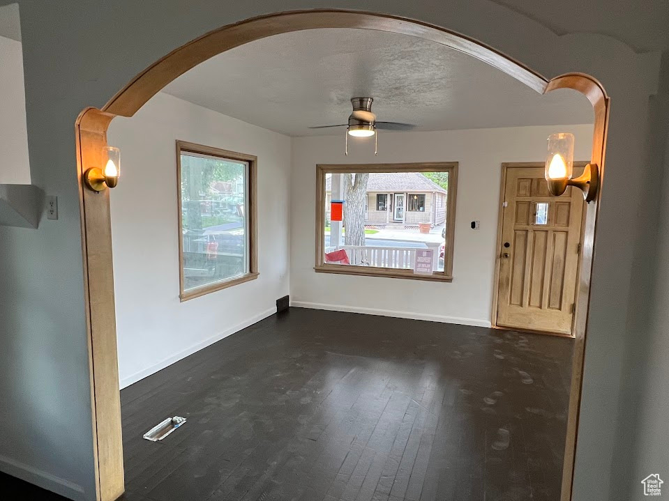 Unfurnished dining area with arched walkways, healthy amount of natural light, a ceiling fan, and dark wood-style flooring