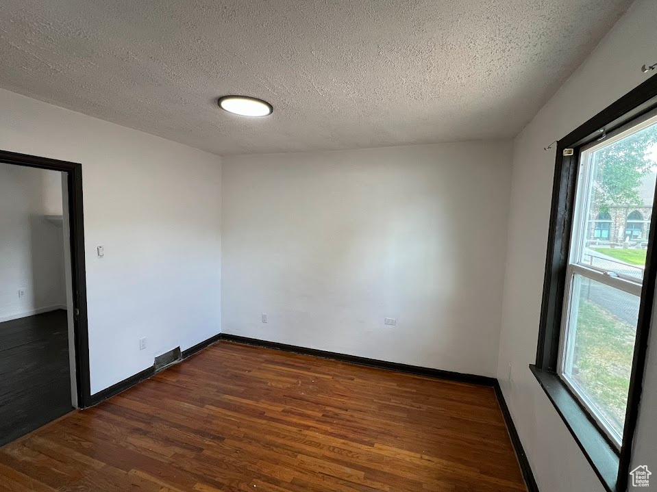 Unfurnished room with dark wood finished floors, plenty of natural light, and a textured ceiling