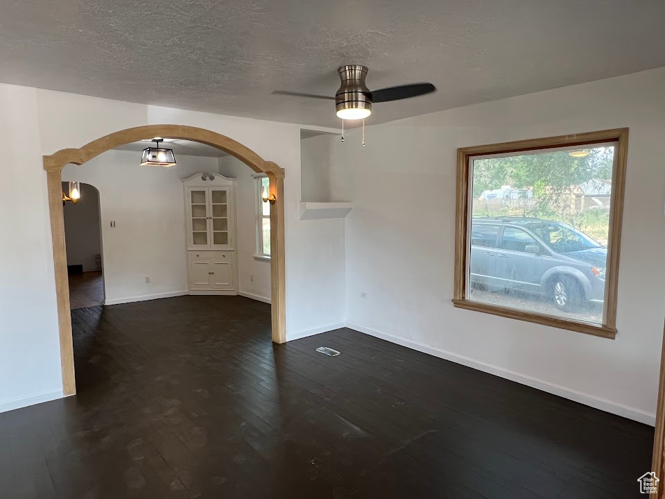 Unfurnished room with arched walkways, ceiling fan, dark wood-style floors, and a textured ceiling