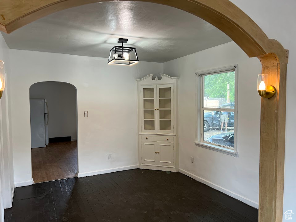 Unfurnished dining area featuring arched walkways and dark wood finished floors