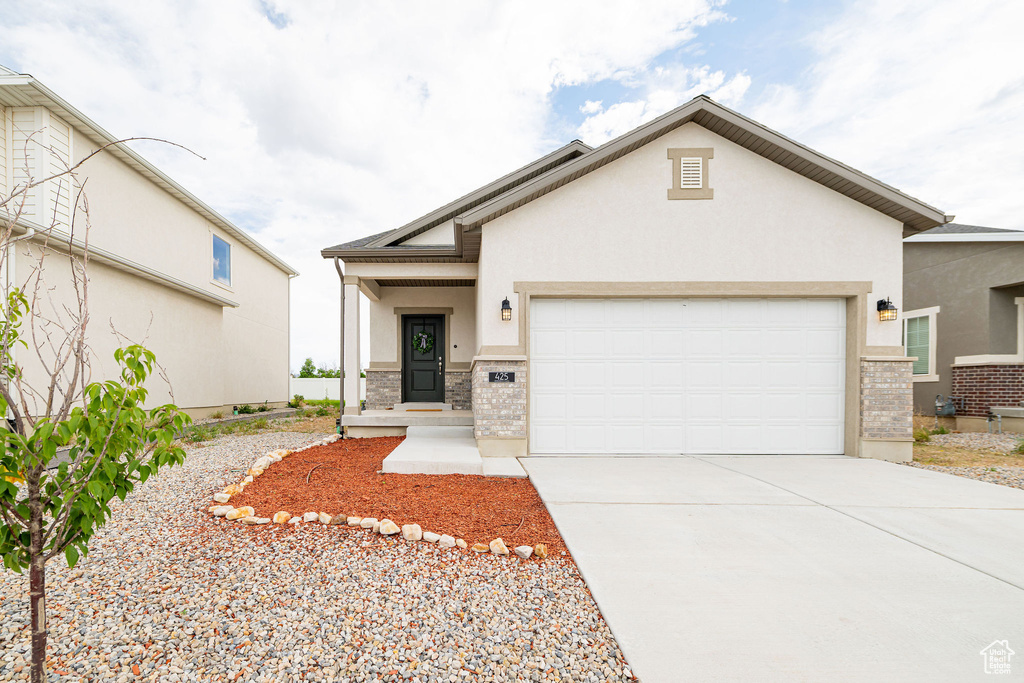 View of front of house featuring brick siding, a garage, stucco siding, and driveway