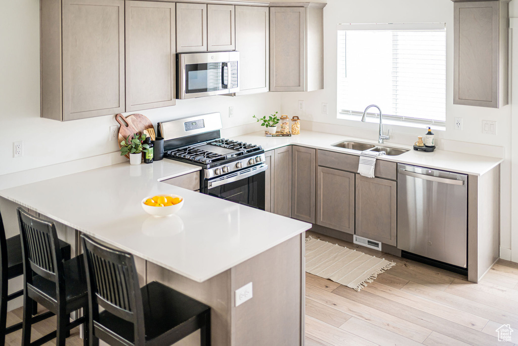 Kitchen with stainless steel appliances, a peninsula, light wood-style floors, a breakfast bar, and light countertops