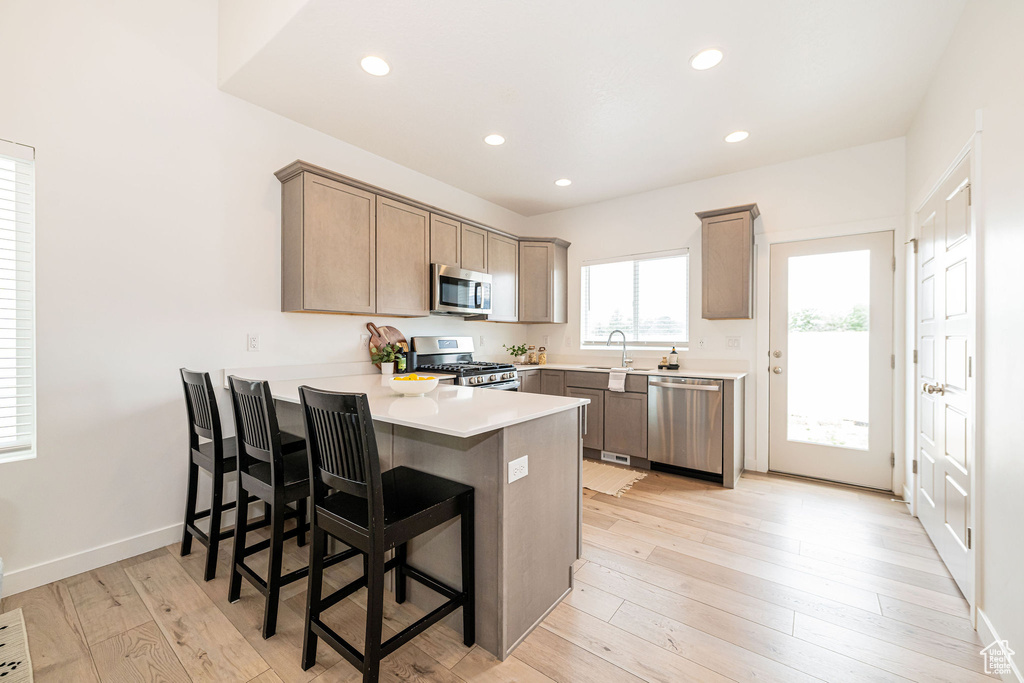 Kitchen with stainless steel appliances, a peninsula, recessed lighting, light countertops, and a kitchen bar