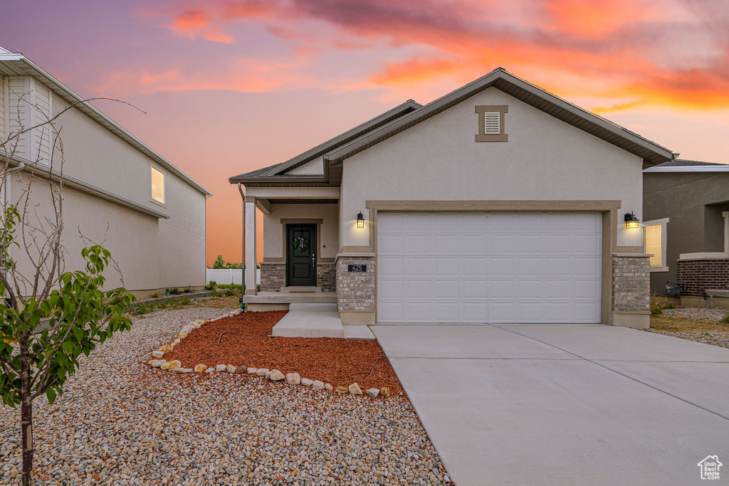 View of front of home with stucco siding, an attached garage, driveway, brick siding, and stone siding