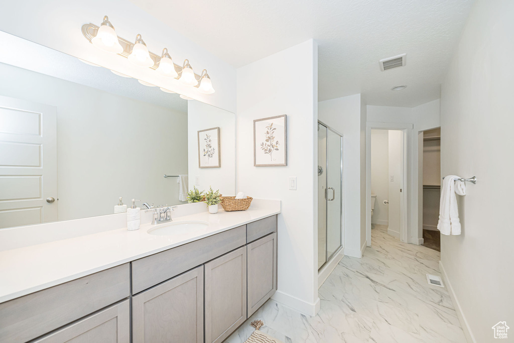 Full bathroom featuring marble finish floors, vanity, a shower stall, and a walk in closet