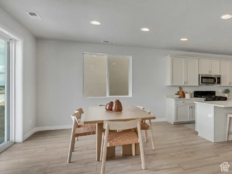 Kitchen with stainless steel microwave, stove, light wood-type flooring, a breakfast bar area, and recessed lighting