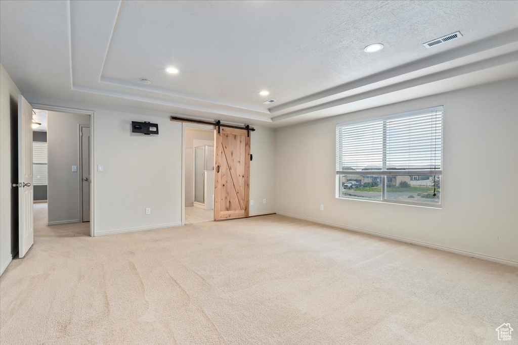 Unfurnished bedroom with a raised ceiling, light colored carpet, recessed lighting, a barn door, and connected bathroom