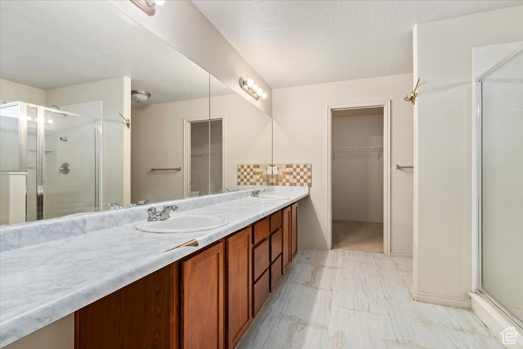 Full bath featuring a walk in closet, a stall shower, double vanity, and a textured ceiling