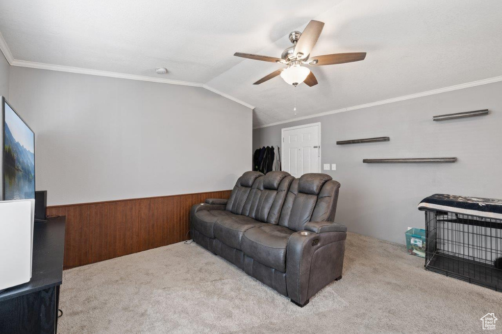 Living area featuring a ceiling fan, carpet flooring, wainscoting, wooden walls, and ornamental molding