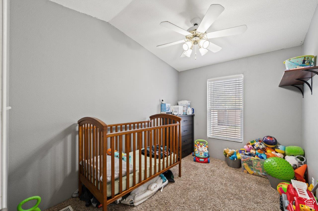 Bedroom featuring carpet floors, a crib, vaulted ceiling, and ceiling fan