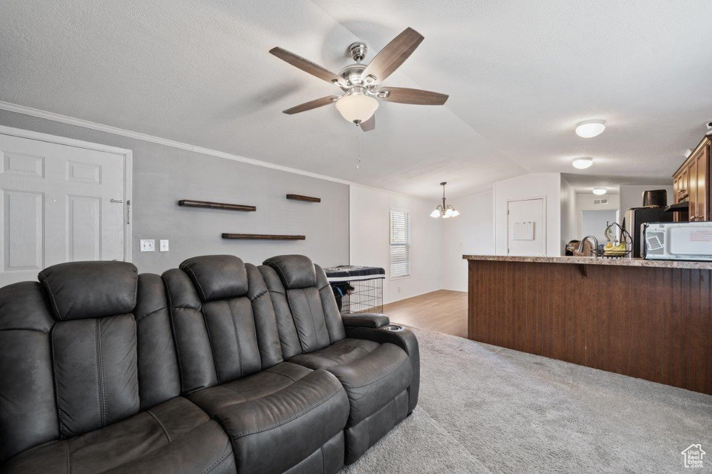Living area featuring a chandelier, lofted ceiling, ceiling fan, and light carpet