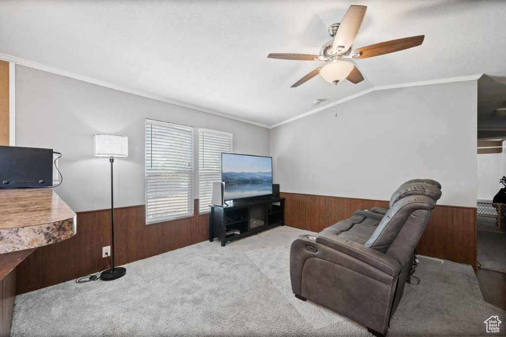 Carpeted living room with a wainscoted wall, wood walls, crown molding, ceiling fan, and vaulted ceiling