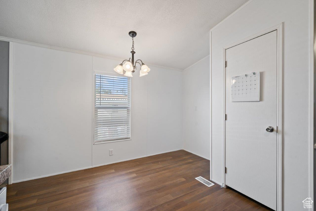 Unfurnished dining area with a chandelier, dark wood-type flooring, and ornamental molding