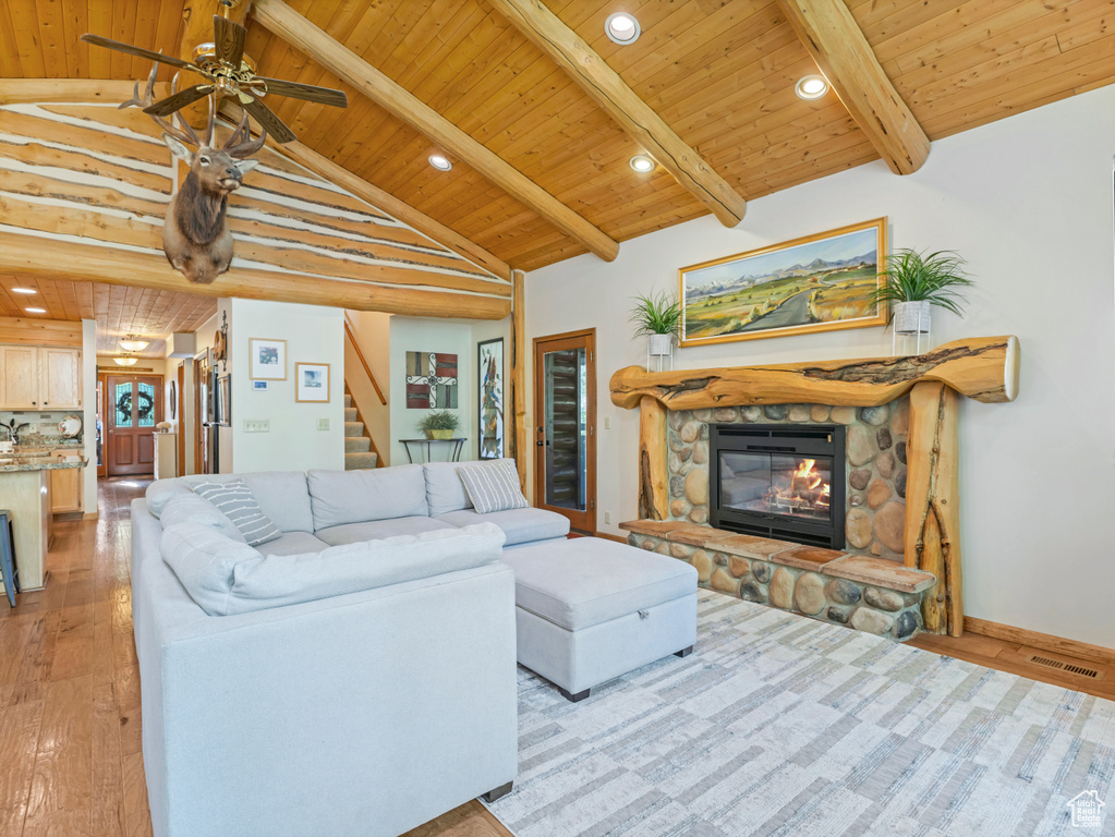 Living room with a wooden ceiling with exposed beams, light wood-type flooring, stairs, a fireplace, and ceiling fan