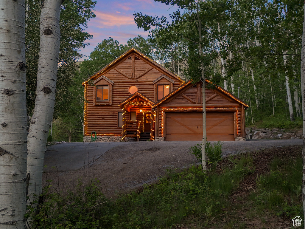 Log cabin featuring driveway, an attached garage, and log exterior