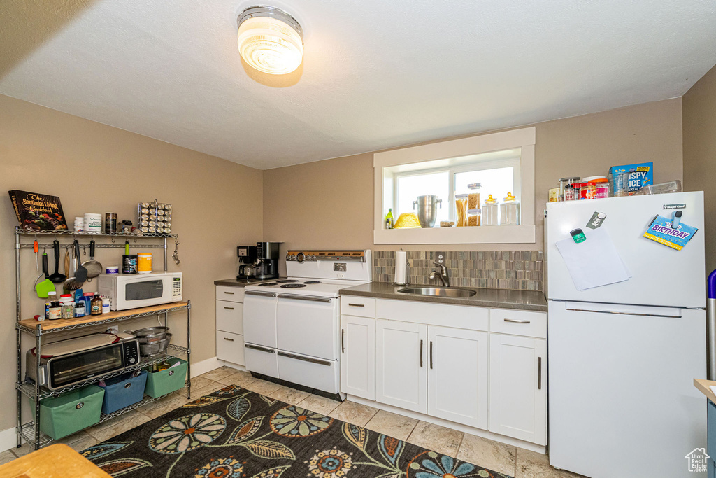 Kitchen with white appliances, white cabinetry, light tile patterned floors, and tasteful backsplash