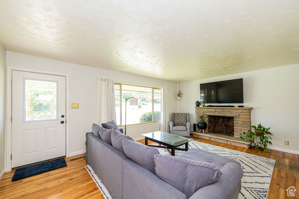 Living room featuring a stone fireplace, wood-type flooring, and a textured ceiling