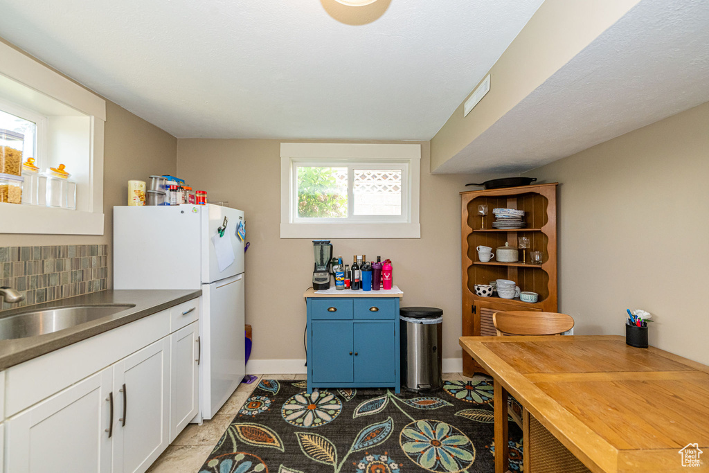 Kitchen with freestanding refrigerator, tasteful backsplash, white cabinets, blue cabinetry, and light tile patterned floors