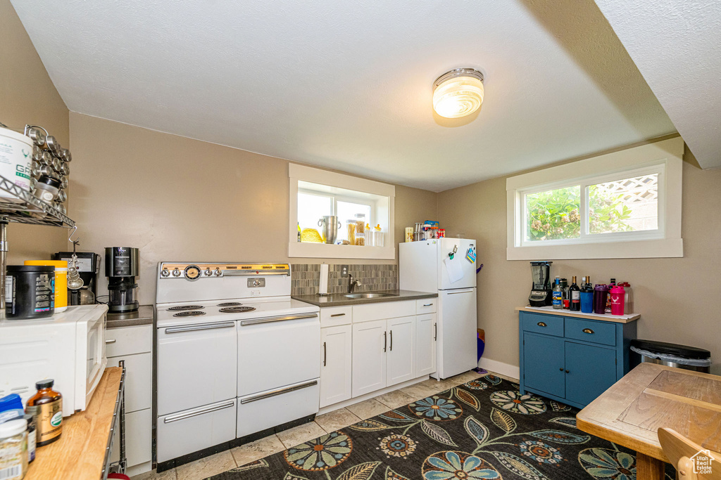 Kitchen featuring white appliances, white cabinets, light tile patterned floors, tasteful backsplash, and blue cabinets