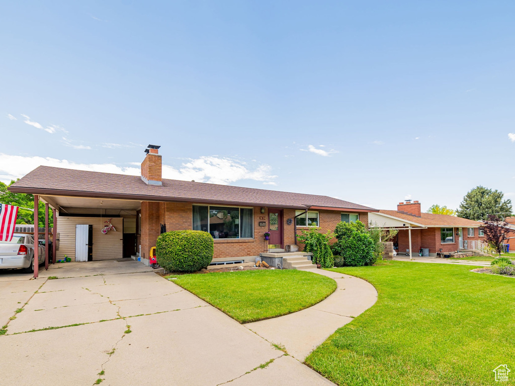 Ranch-style house featuring brick siding, a chimney, a front lawn, driveway, and an attached carport