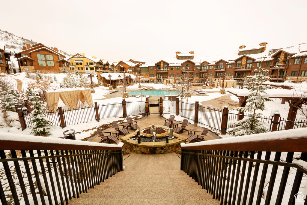 Snow covered back of property featuring a residential view, a fire pit, view of pool, and a patio area