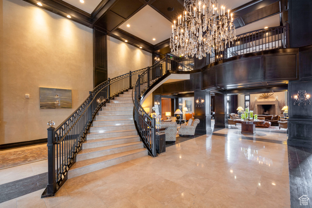 Stairway featuring a towering ceiling, a chandelier, beam ceiling, coffered ceiling, and a fireplace