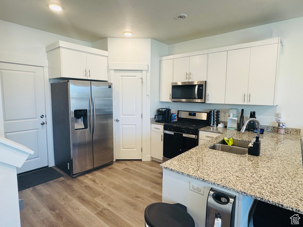 Kitchen with appliances with stainless steel finishes, light stone countertops, white cabinets, and recessed lighting