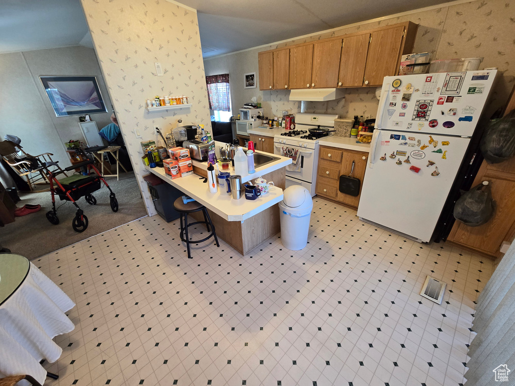 Kitchen featuring white appliances, under cabinet range hood, light countertops, a kitchen breakfast bar, and light flooring