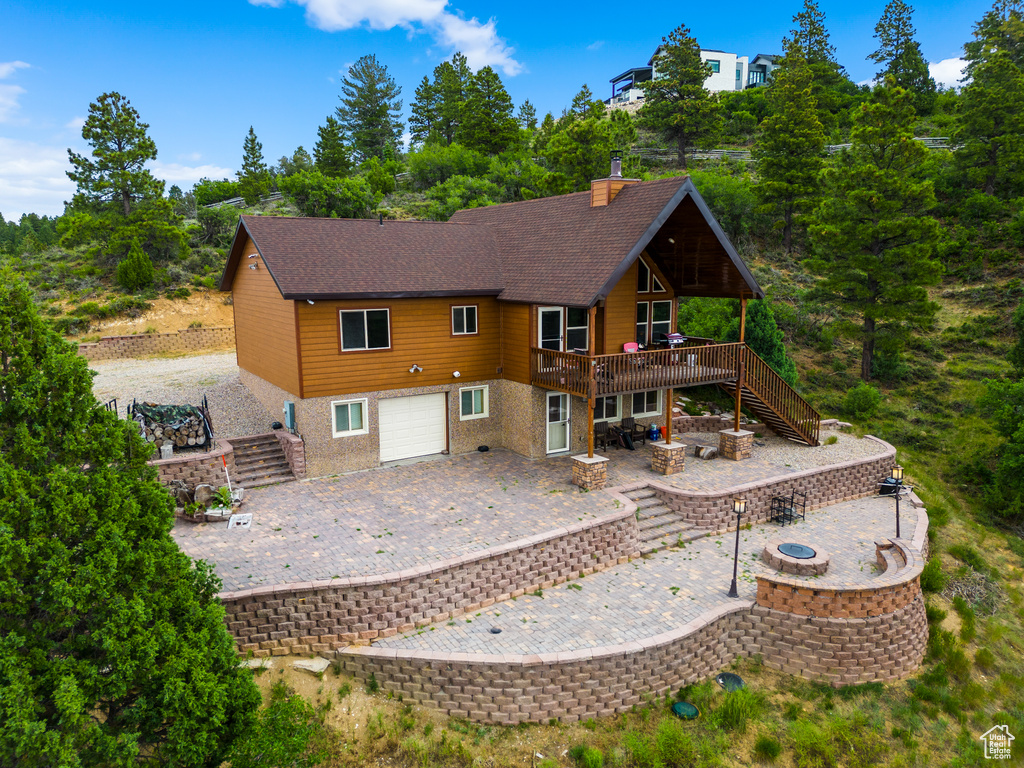 Back of property featuring a fire pit, an attached garage, a patio, stairway, and a deck