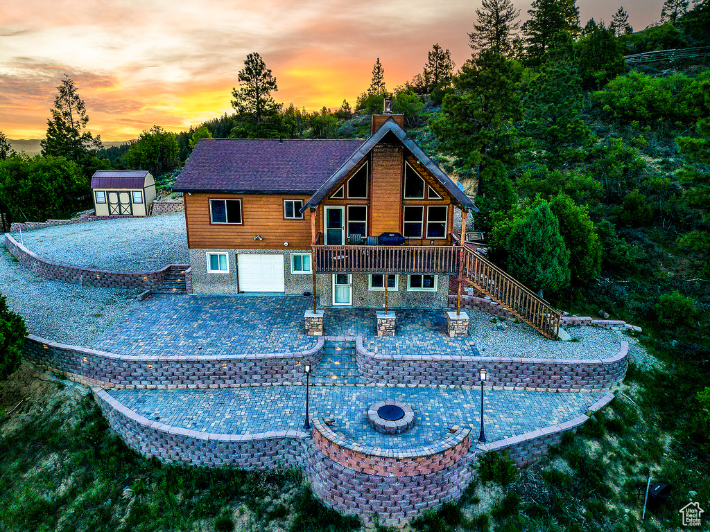 Back of property at dusk featuring a fire pit, stairs, a patio area, driveway, and a chimney
