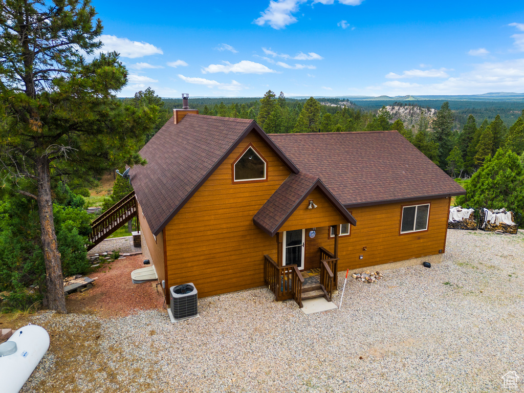 Rustic home with a shingled roof, a wooded view, stairway, and a chimney