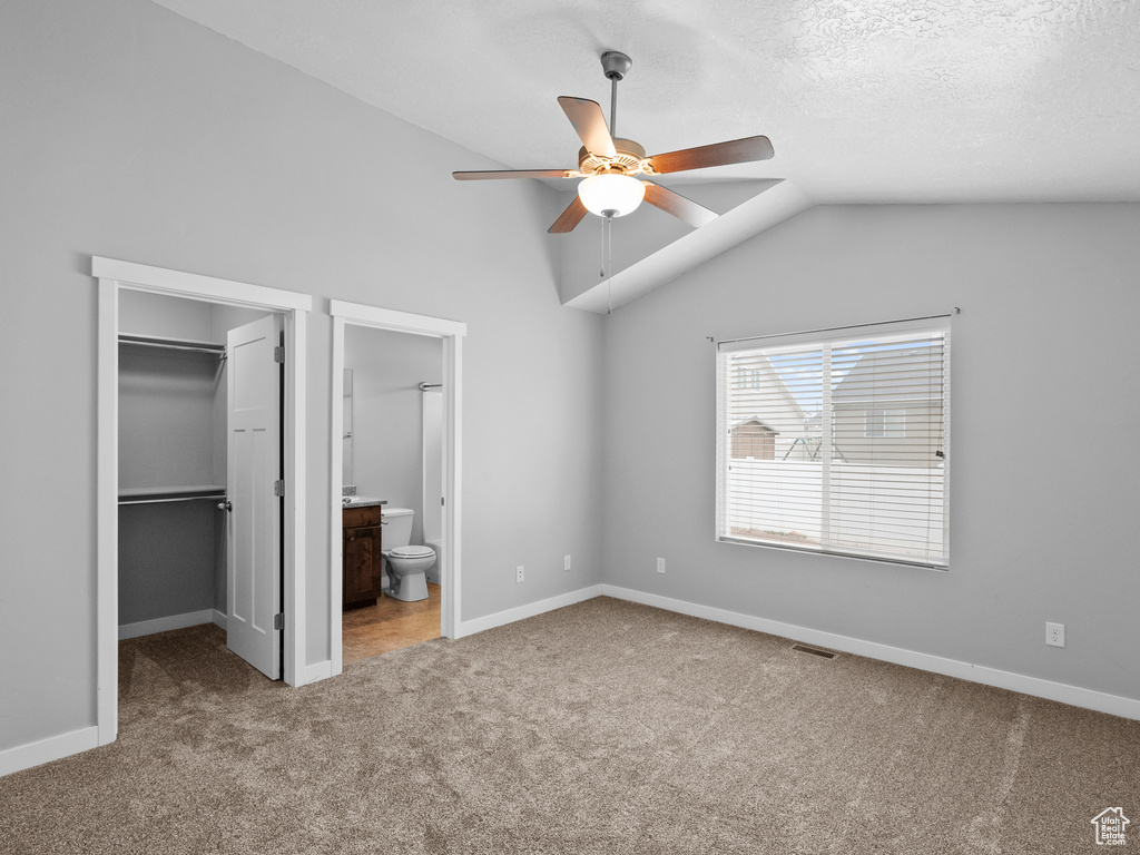 Unfurnished bedroom featuring carpet, a walk in closet, vaulted ceiling, ensuite bath, and a closet